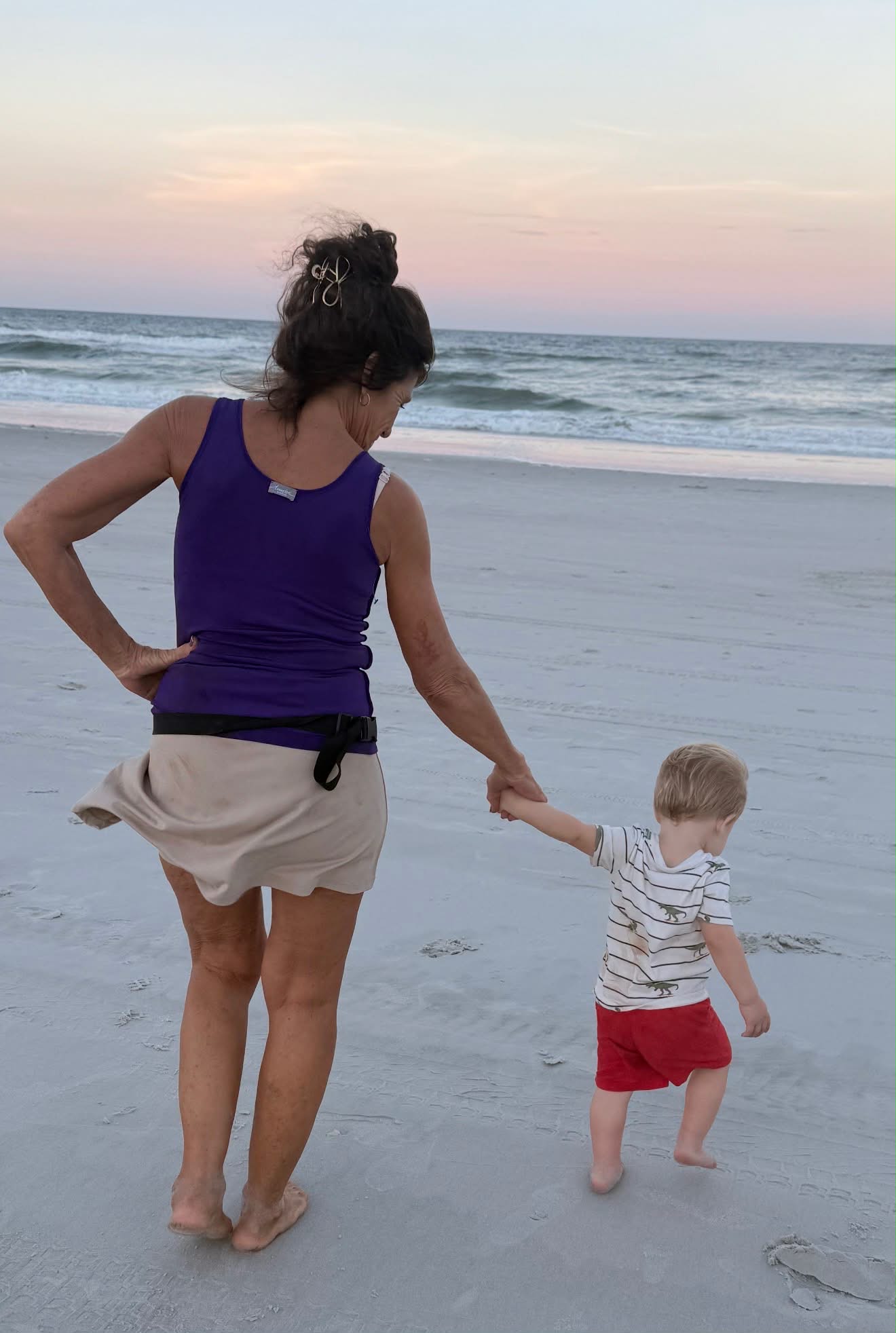 A grandmother and young child walking together on the beach at sunset