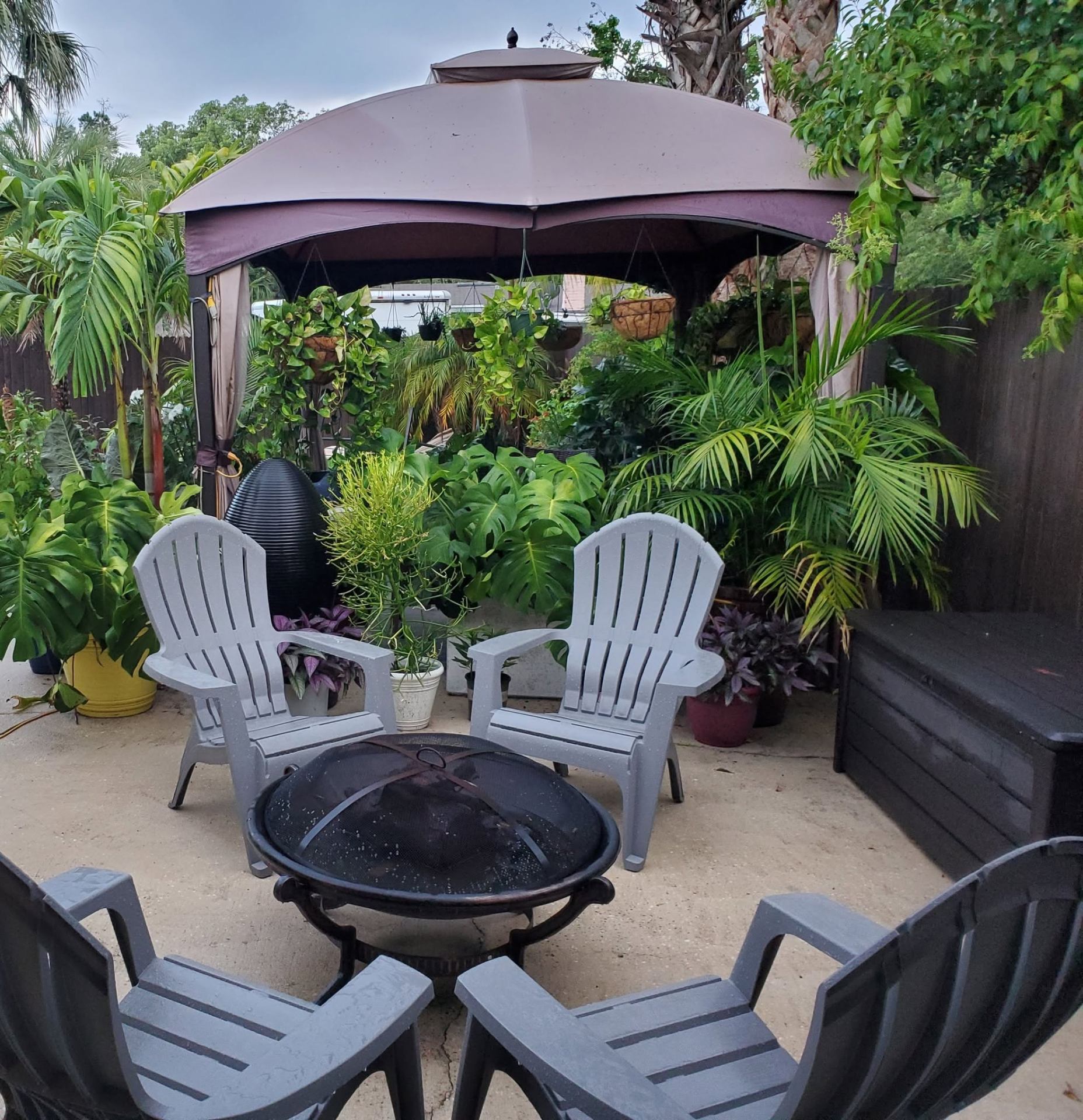Private firepit lounge surrounded by tropical plants and Adirondack chairs